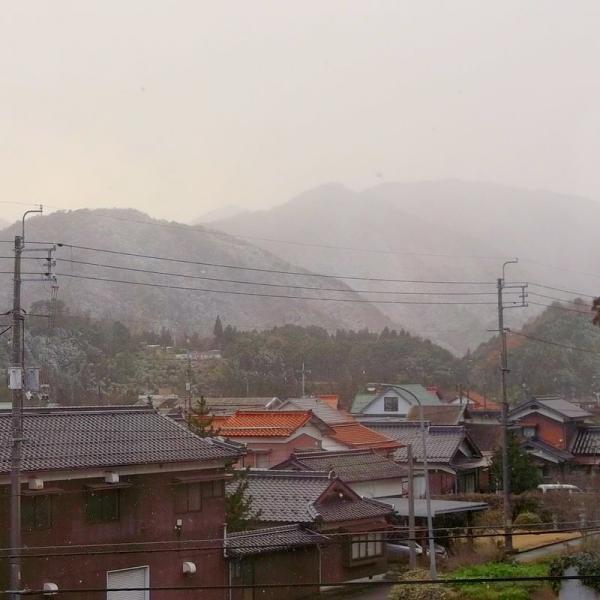 近くに家、遠くに鹿野の山が写っています。雪が降っています。