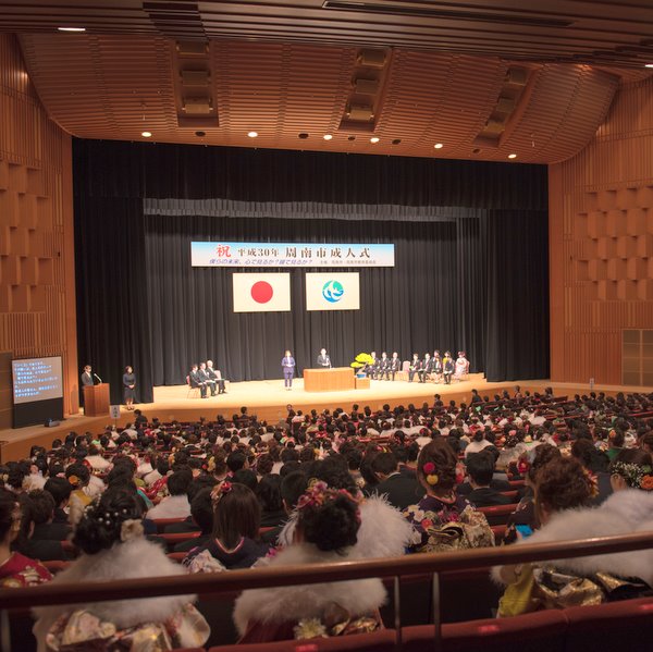 文化会館の屋内写真です。成人式会場内の様子です。客席にほぼ満席の新成人とステージ上に複数の人が写っています。