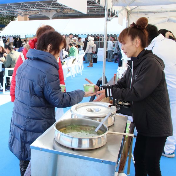 屋外にて、紙の容器にはいった飲食物を手渡している様子の写真です。