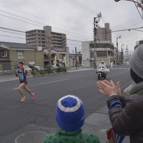 駅伝選手と白バイ、応援する人が写っています。